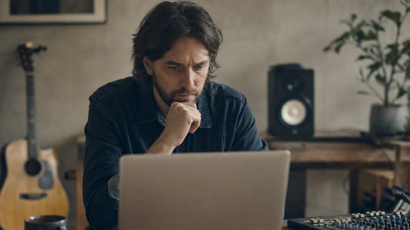 An independent artist reviewing streaming analytics on a laptop in a home studio, checking for irregular activity