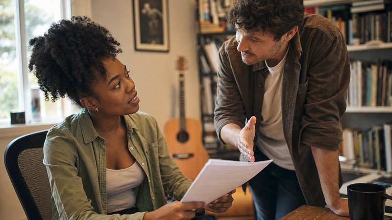 Two songwriters in a home studio setting reviewing documents in an active conversation