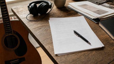 A songwriter reviewing a royalty statement at a desk with a laptop and notebook