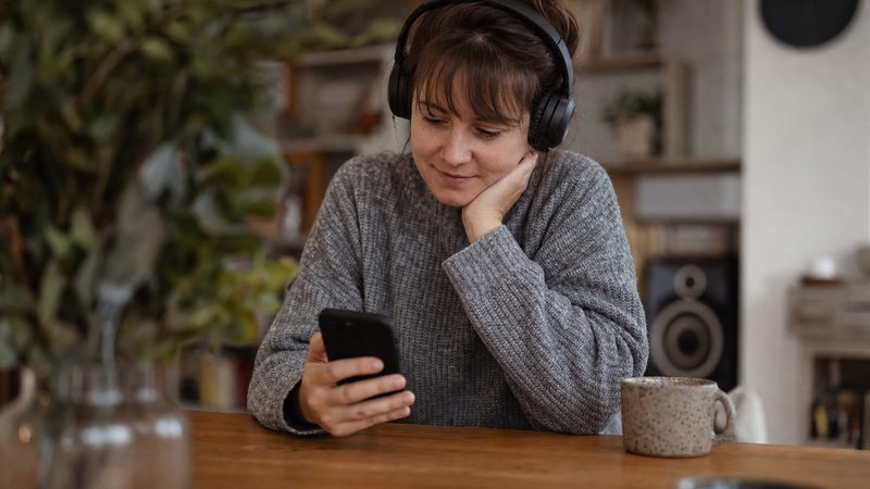 A listener viewing a personalized music playlist on a phone with headphones on a wooden table